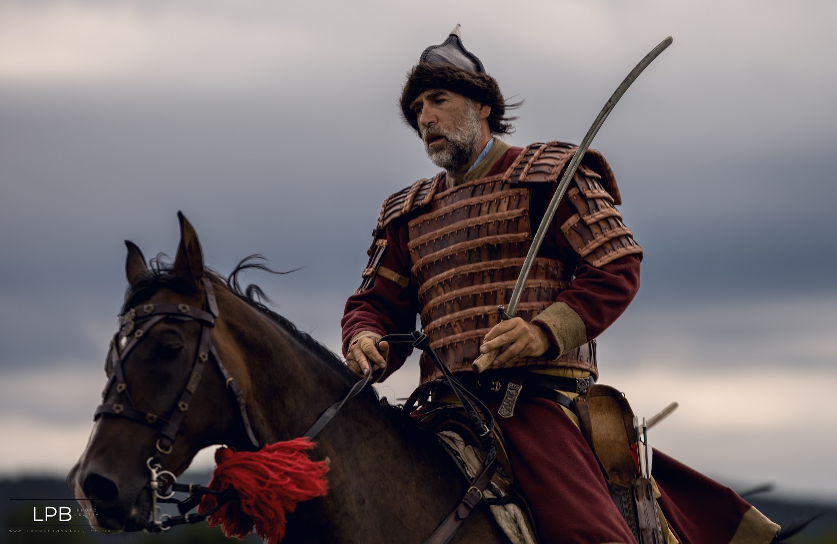 A bearded warrior on a bay horse against a grey sky