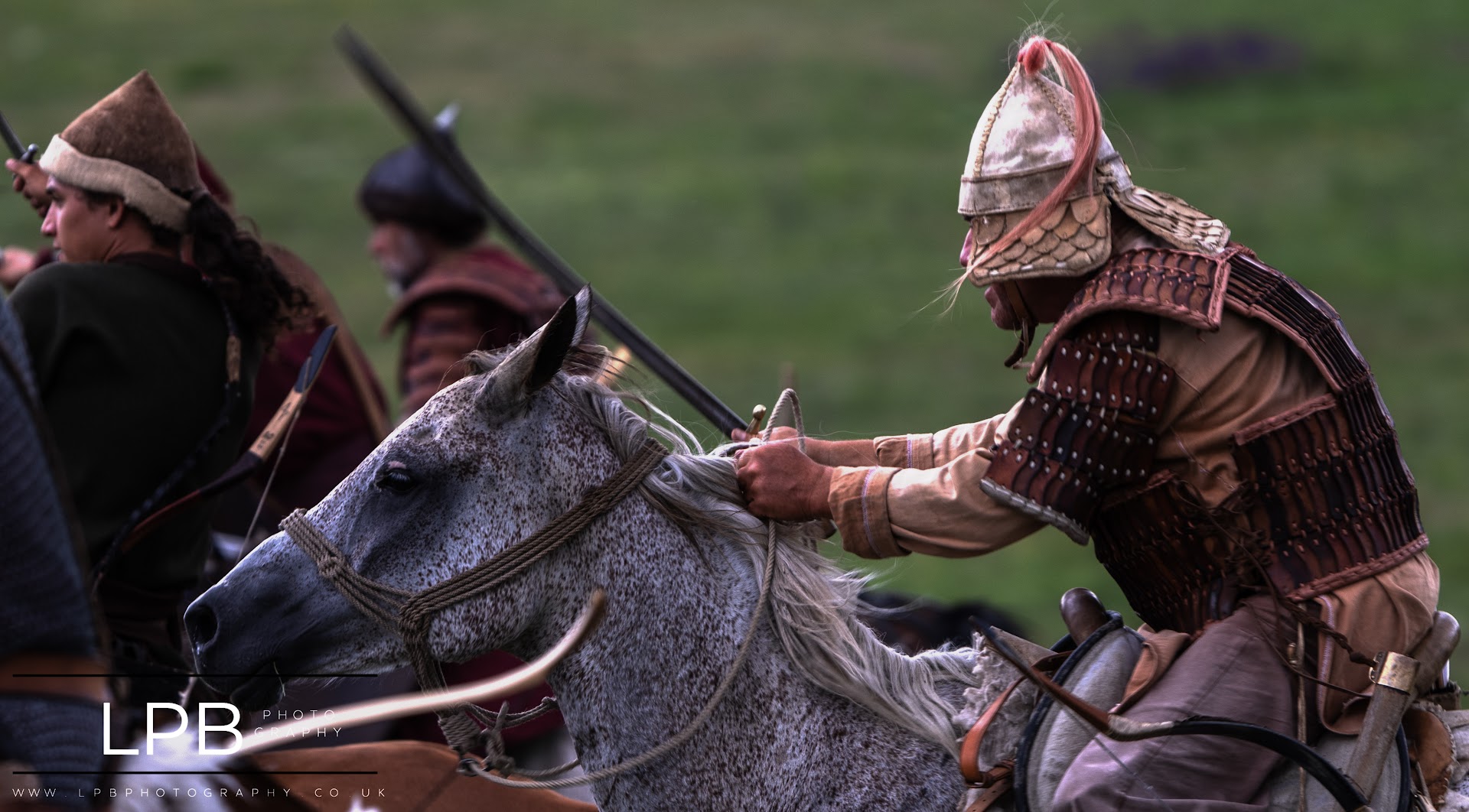 An armoured rider gripping a white horse's mane, sabre raised