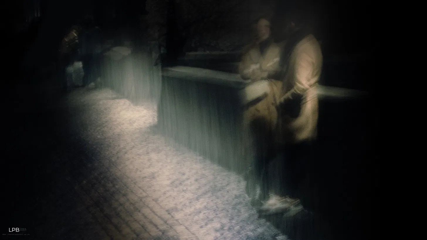 A figure leaning on a bridge wall at night, light streaming like rain